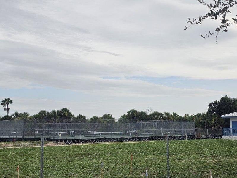 Empty outdoor bleachers beside a fenced grassy field under a cloudy sky