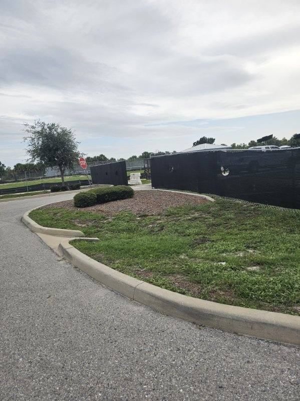 Curved sidewalk beside a grassy berm and black fence under a cloudy sky.