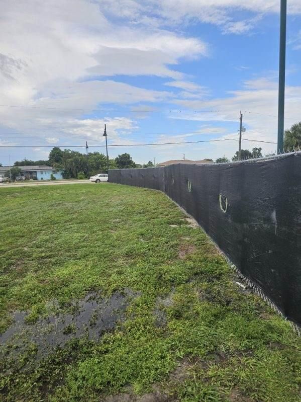 Grassy roadside beside a black fence under a cloudy sky with utility poles in the distance