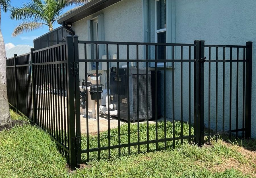 Black metal fence beside a white house with outdoor AC units and green grass