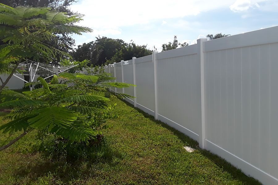 White fence along a grassy yard beside a tree under a cloudy sky