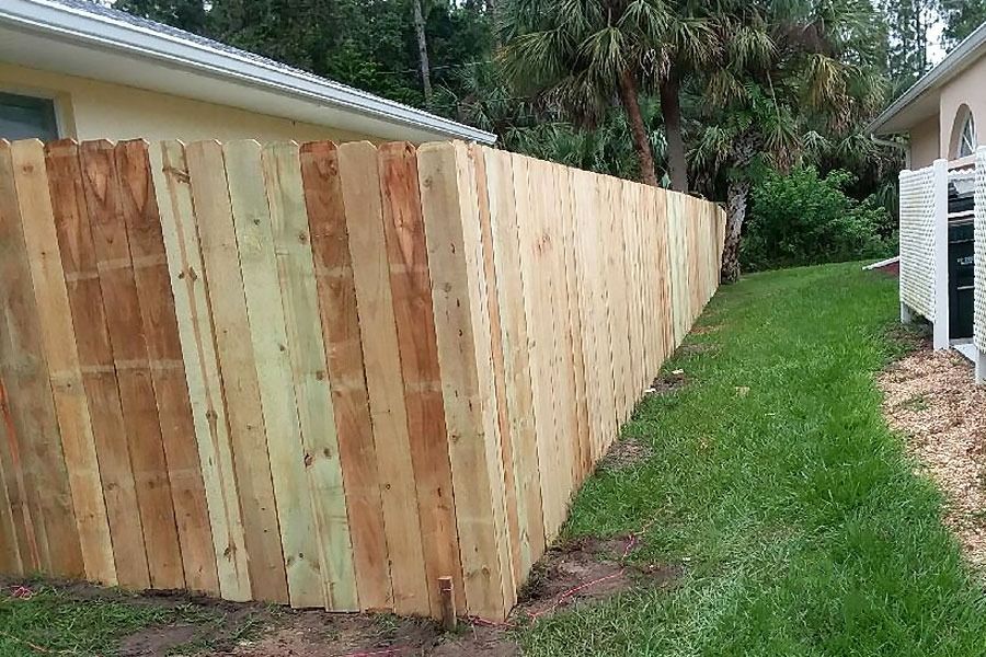 Wooden privacy fence along a grassy side yard beside a house and trees
