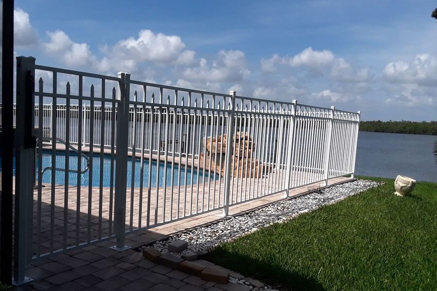 White metal fence beside a blue pool overlooking a lake under a cloudy sky
