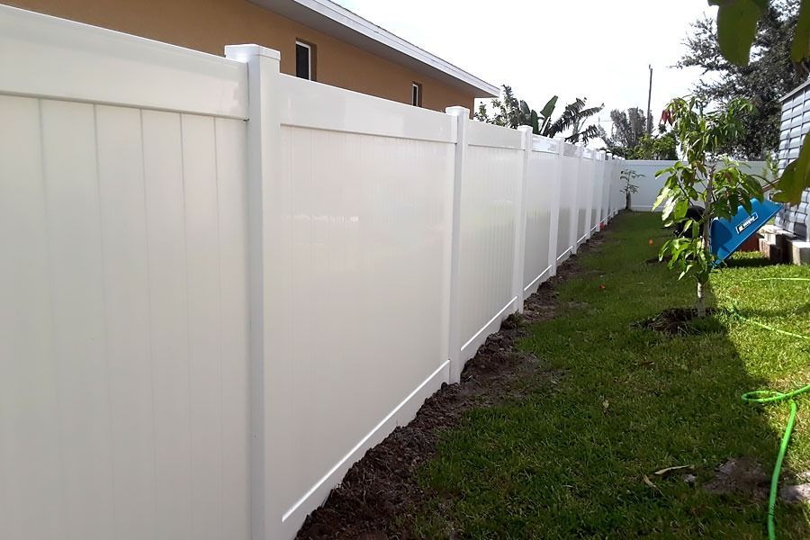 White vinyl fence along a grassy yard beside a house, receding into the distance