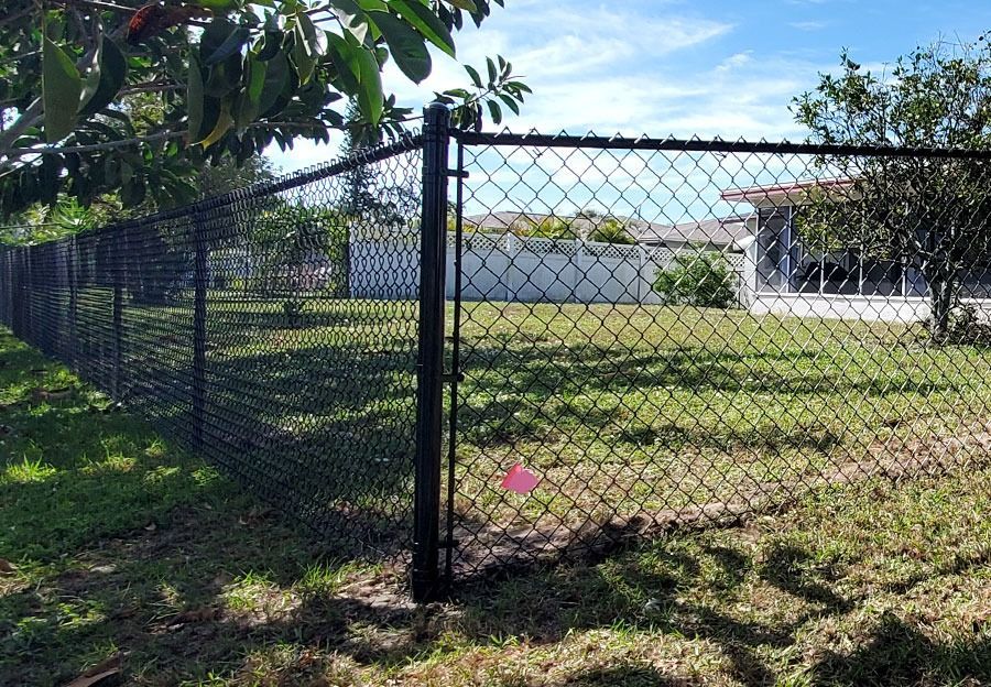 Black chain-link fence around a grassy yard with a house in the background and a pink marker near the ground