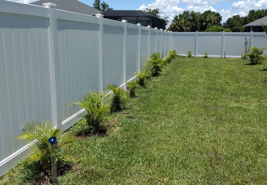 White vinyl fence lining a grassy yard with small shrubs on a sunny day