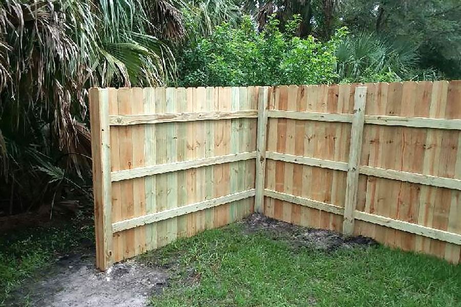 Wooden corner fence in a grassy backyard with trees behind it