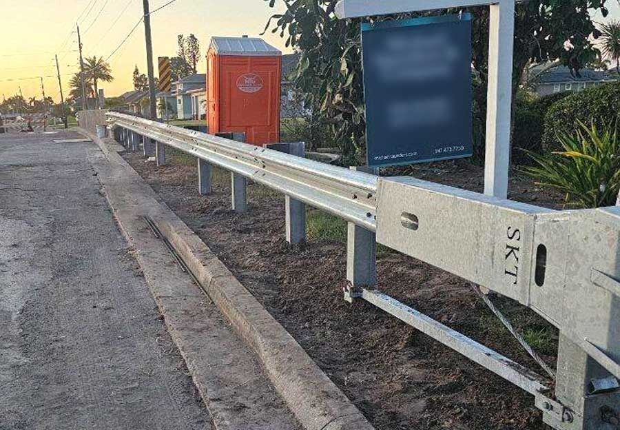 Roadside guardrail beside a sidewalk at sunset, with orange and blue utility boxes nearby