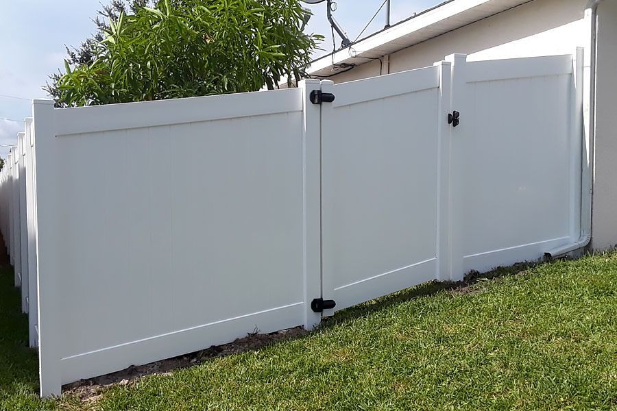 White vinyl fence with a gate beside a grassy lawn and house wall