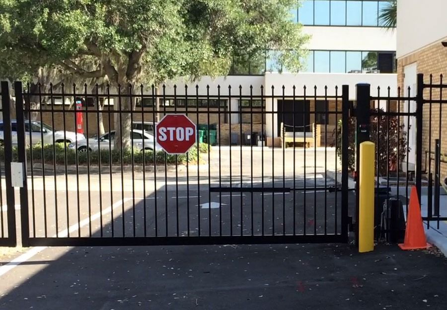 Black metal gate with red stop sign, orange cone, and yellow bollard in front of a building