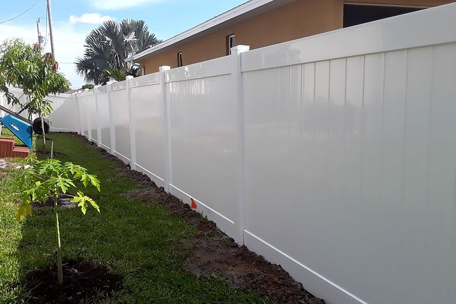 White vinyl fence along a grassy yard beside a house on a sunny day