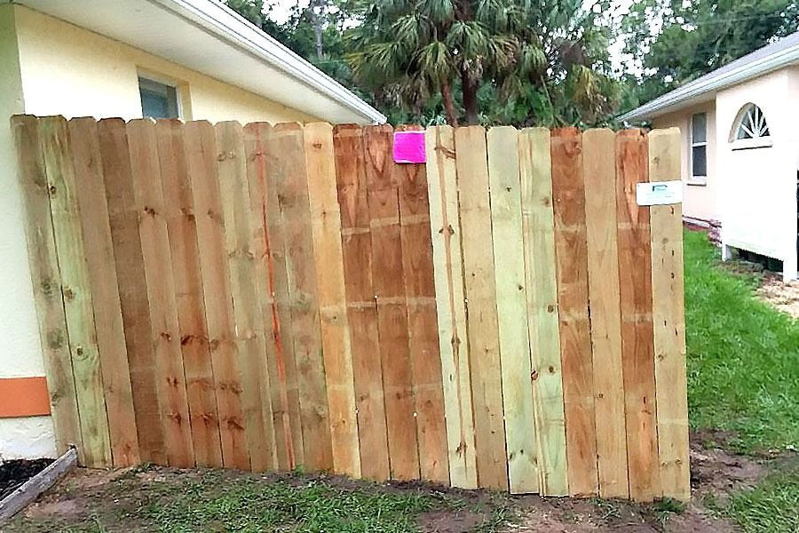 Wooden fence panels beside a house, with a bright pink note near the top and a white sign on the right.