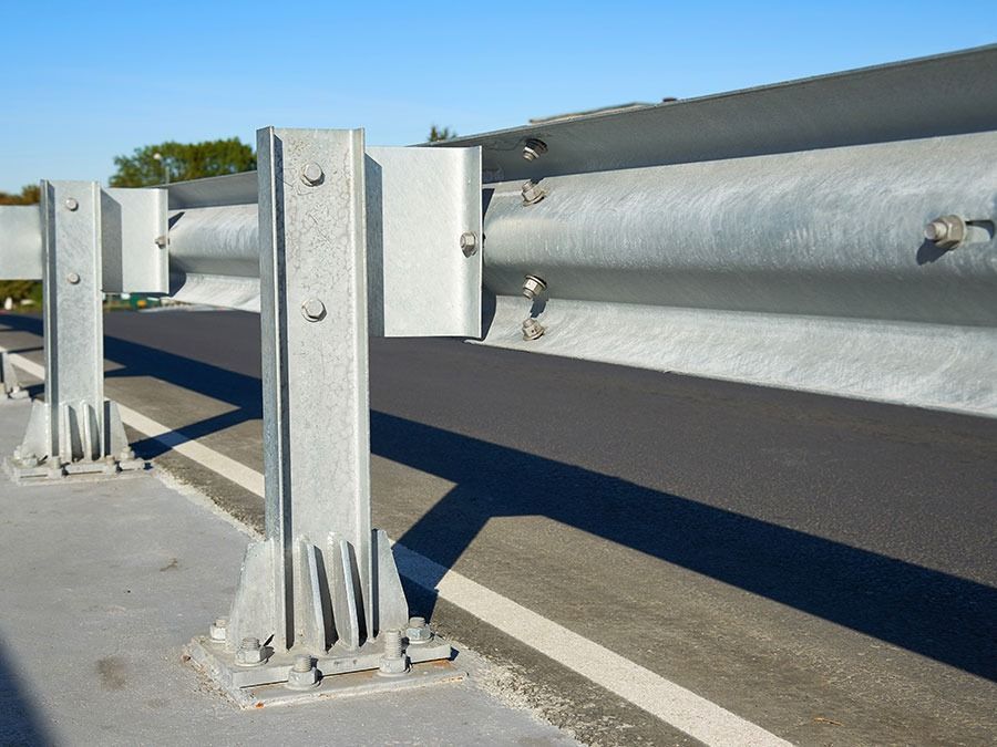 Metal guardrail posts and a horizontal beam mounted on a concrete surface outdoors.