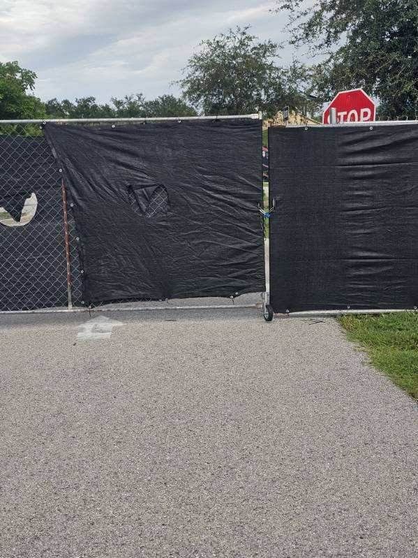 Black tarp fence blocks a paved path near a stop sign and chain-link fence.