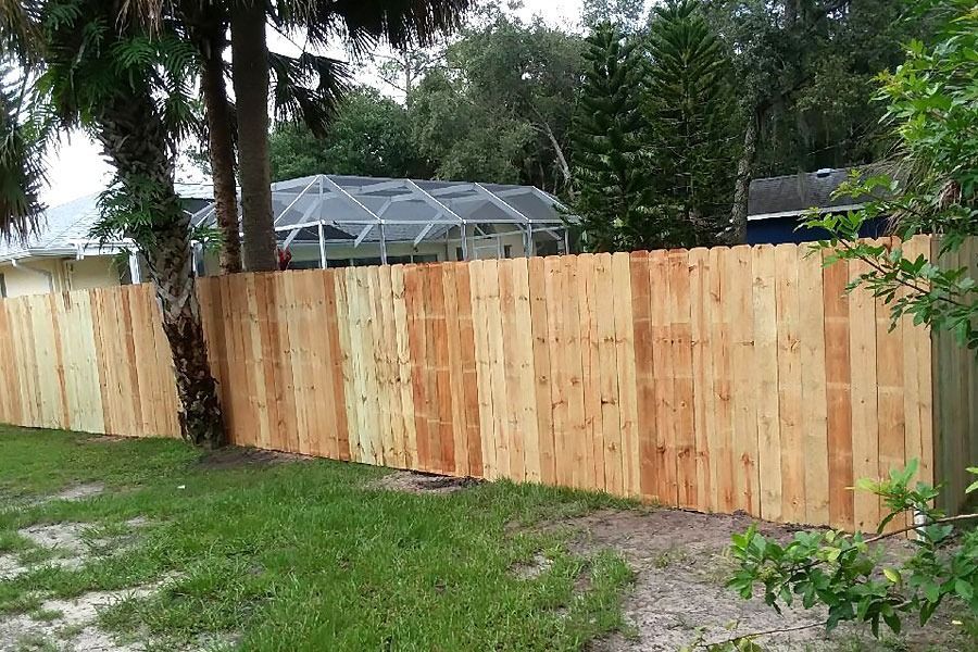 Fresh wooden privacy fence along a grassy yard with trees and a screened pool enclosure in the background
