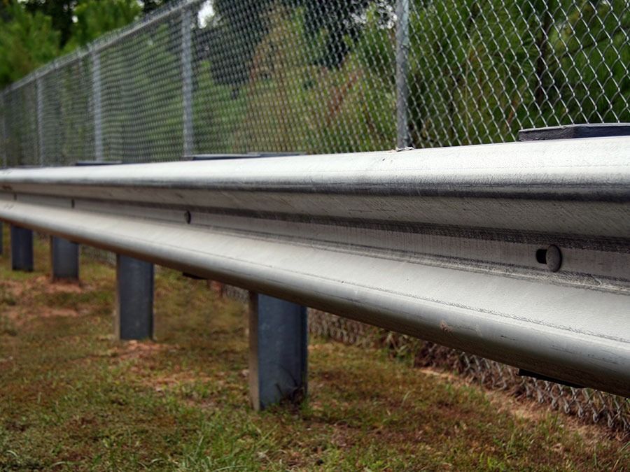 Metal highway guardrail beside a chain-link fence on a grassy roadside