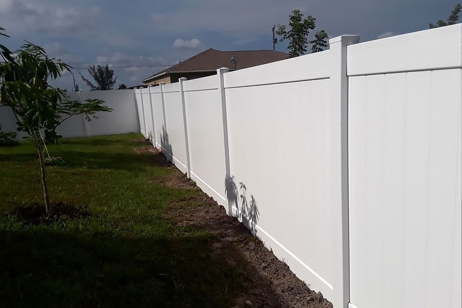 White vinyl fence along a grassy yard under a partly cloudy sky.