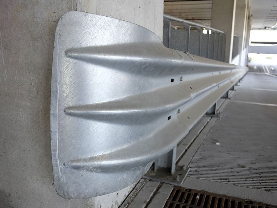 Silver highway guardrail attached to a concrete wall along a covered walkway
