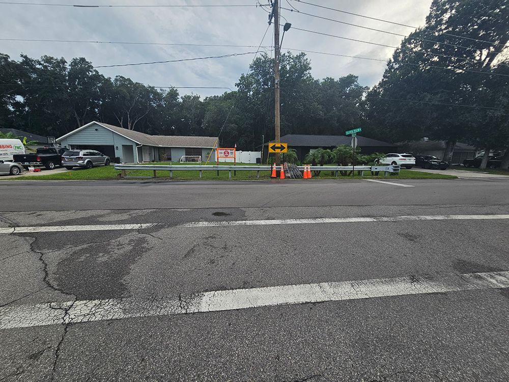 Road with cracked asphalt, orange cones, and a yellow warning sign near a residential street.