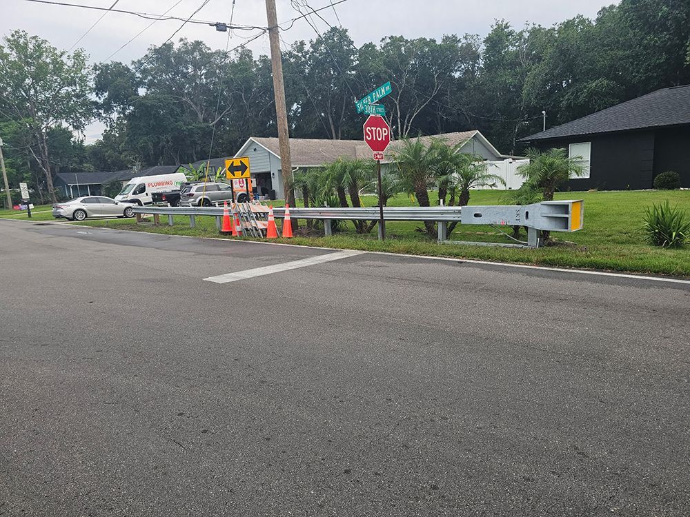 Roadside barrier by a stop sign with orange cones and a utility truck near a house on a cloudy day.