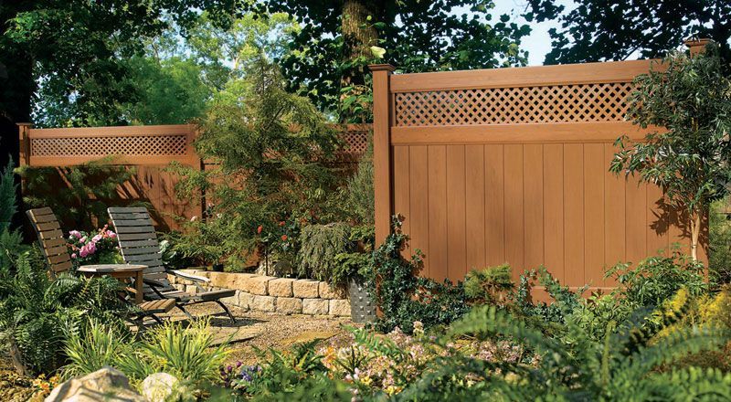 Backyard garden with wooden privacy fence, stone wall, and patio chairs under trees