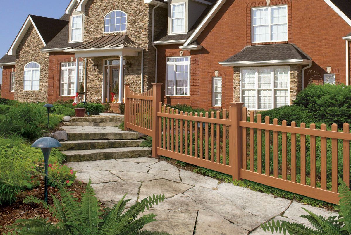 Brick townhouses with front steps, stone path, and wooden picket fence in a landscaped yard