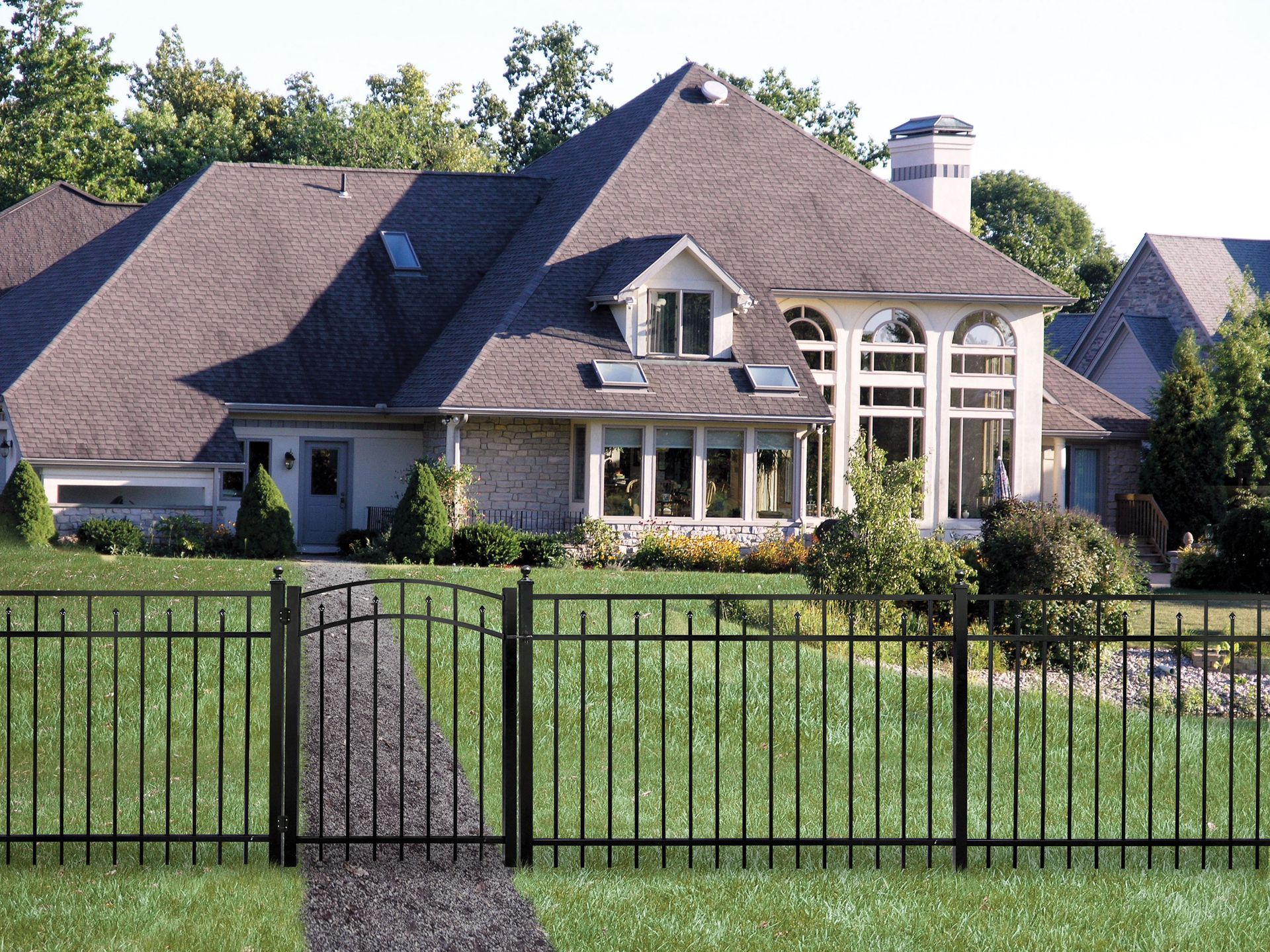 Large suburban house with a dark roof, front lawn, and black metal fence under a clear sky
