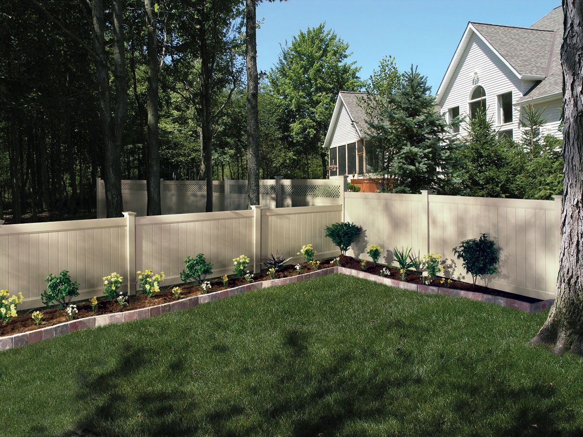 Backyard garden with new flower bed along a beige fence beside a green lawn and houses