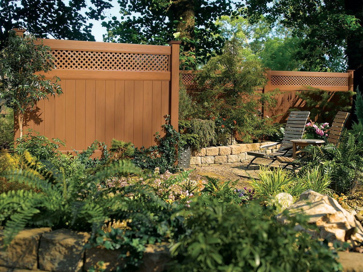 Wooden privacy fence and stone patio with lounge chairs in a lush green garden