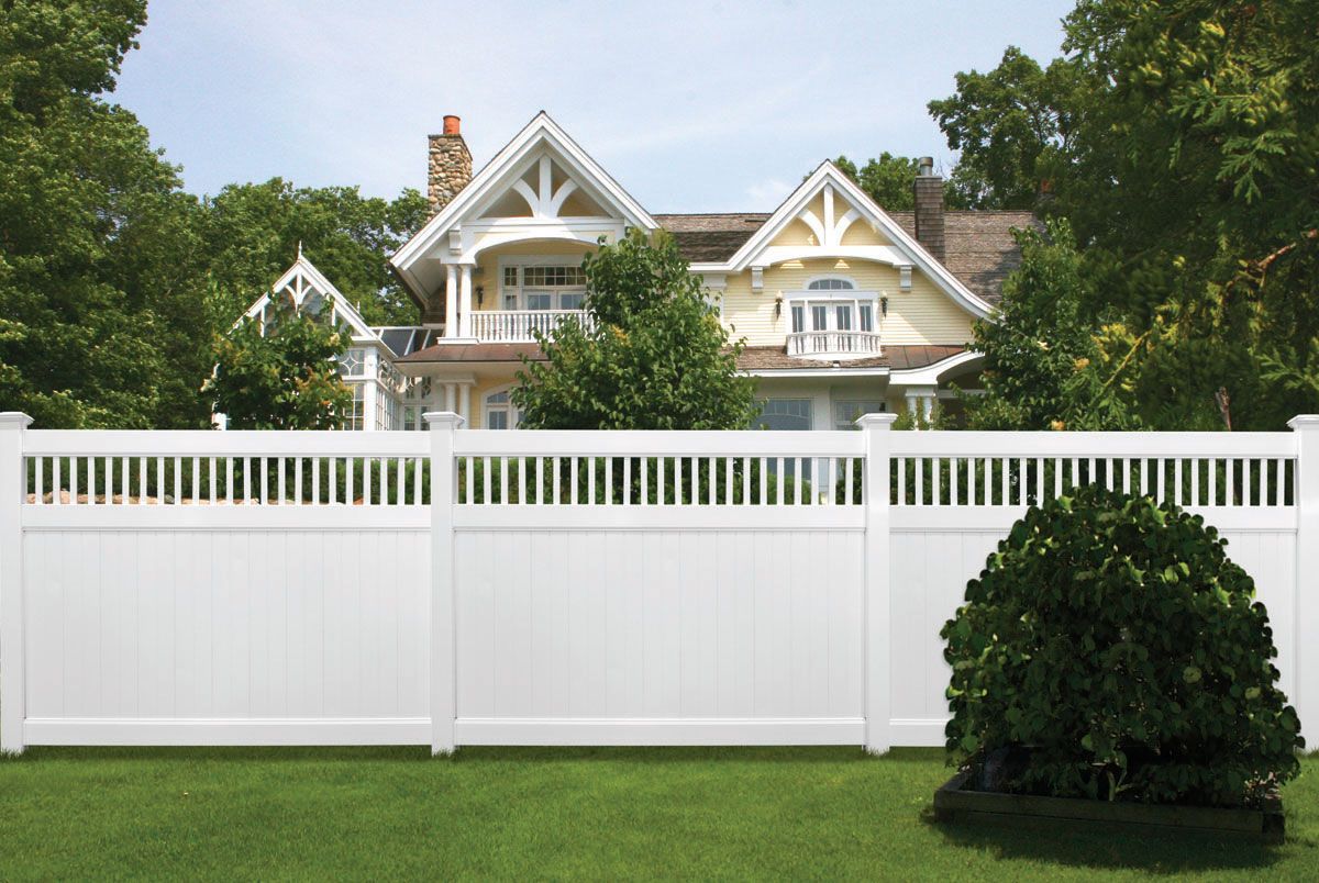 White fence in front of a large beige house with trees and a green lawn