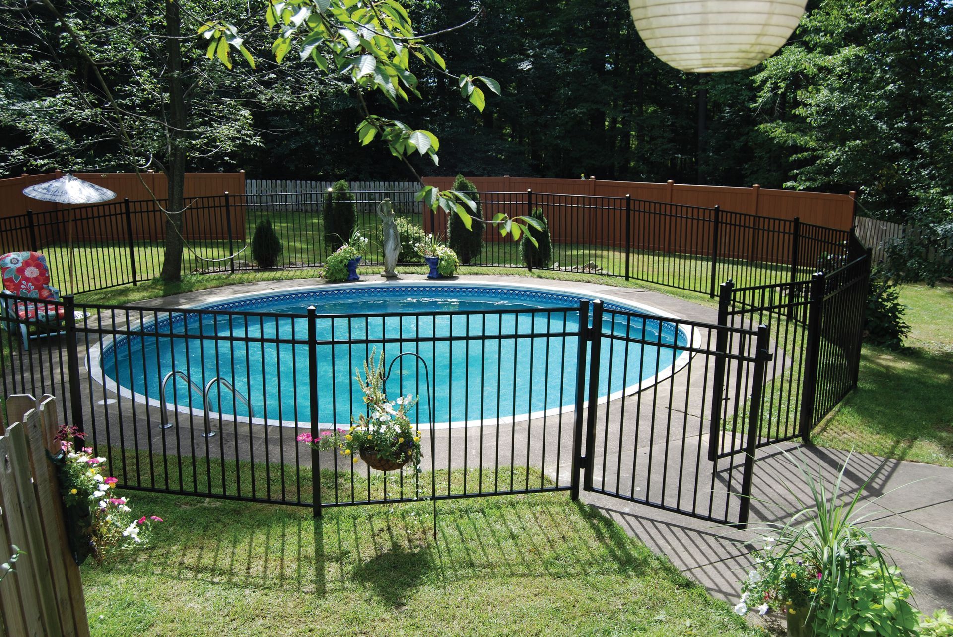 Backyard pool with black fence, green lawn, and trees, viewed through an open gate