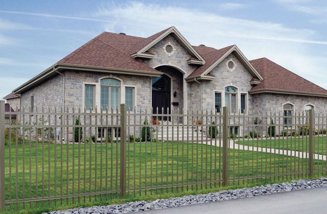 Stone house with red tile roof behind a metal fence on a green lawn