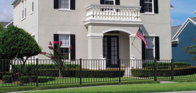 White house with balcony, black fence, and American flag in front of a green lawn