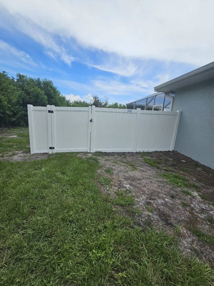 White vinyl gate blocking a grassy side yard beside a gray house under a partly cloudy sky