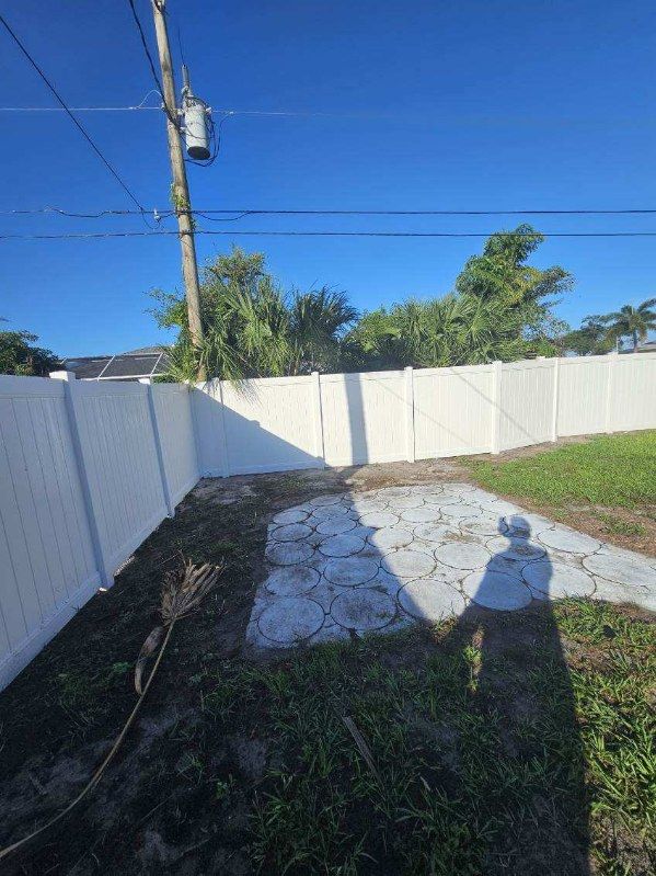 Backyard with white fences, concrete patio, grass, utility pole, and long morning shadows