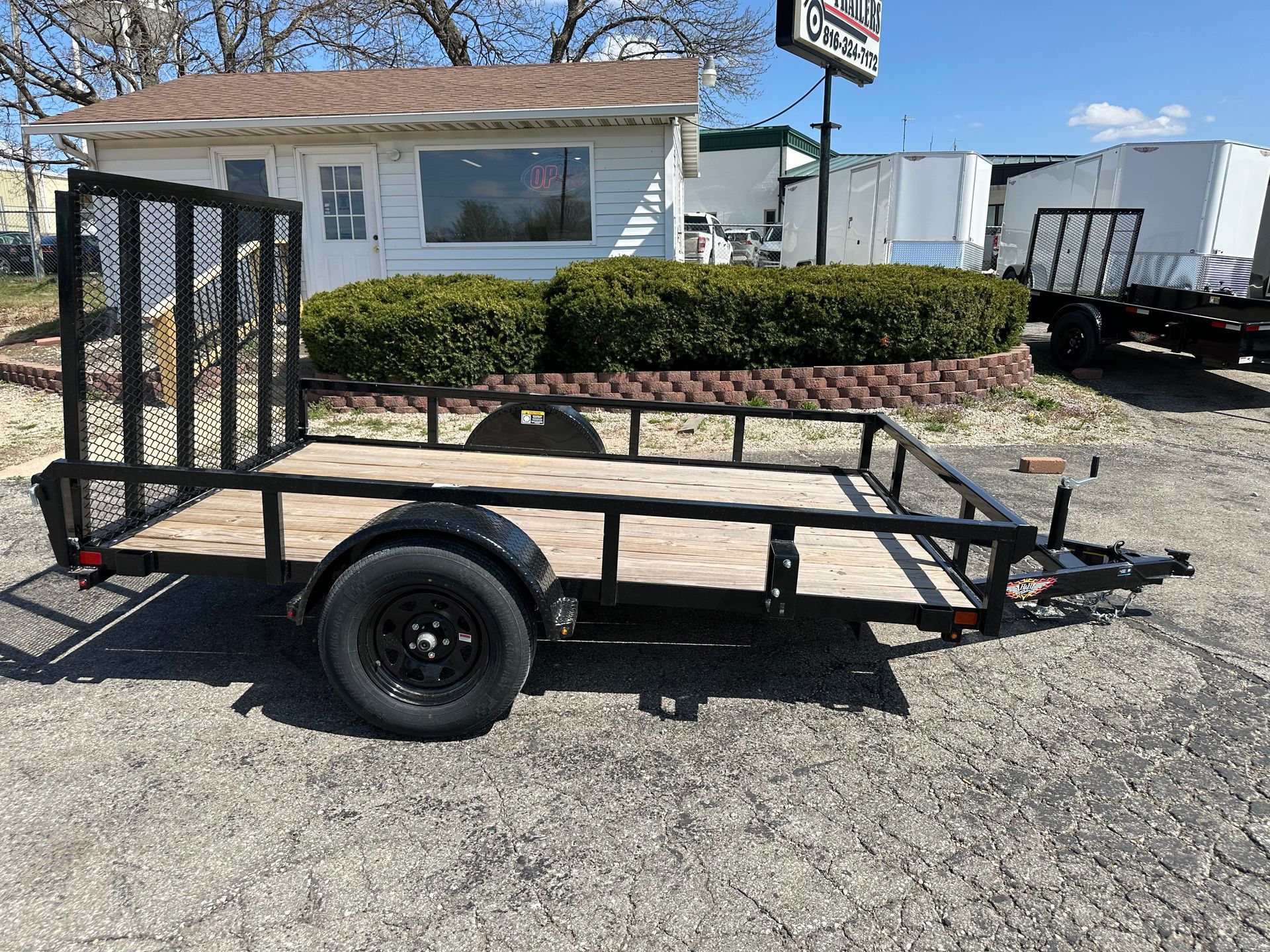A small trailer is parked in the grass on the side of the road.