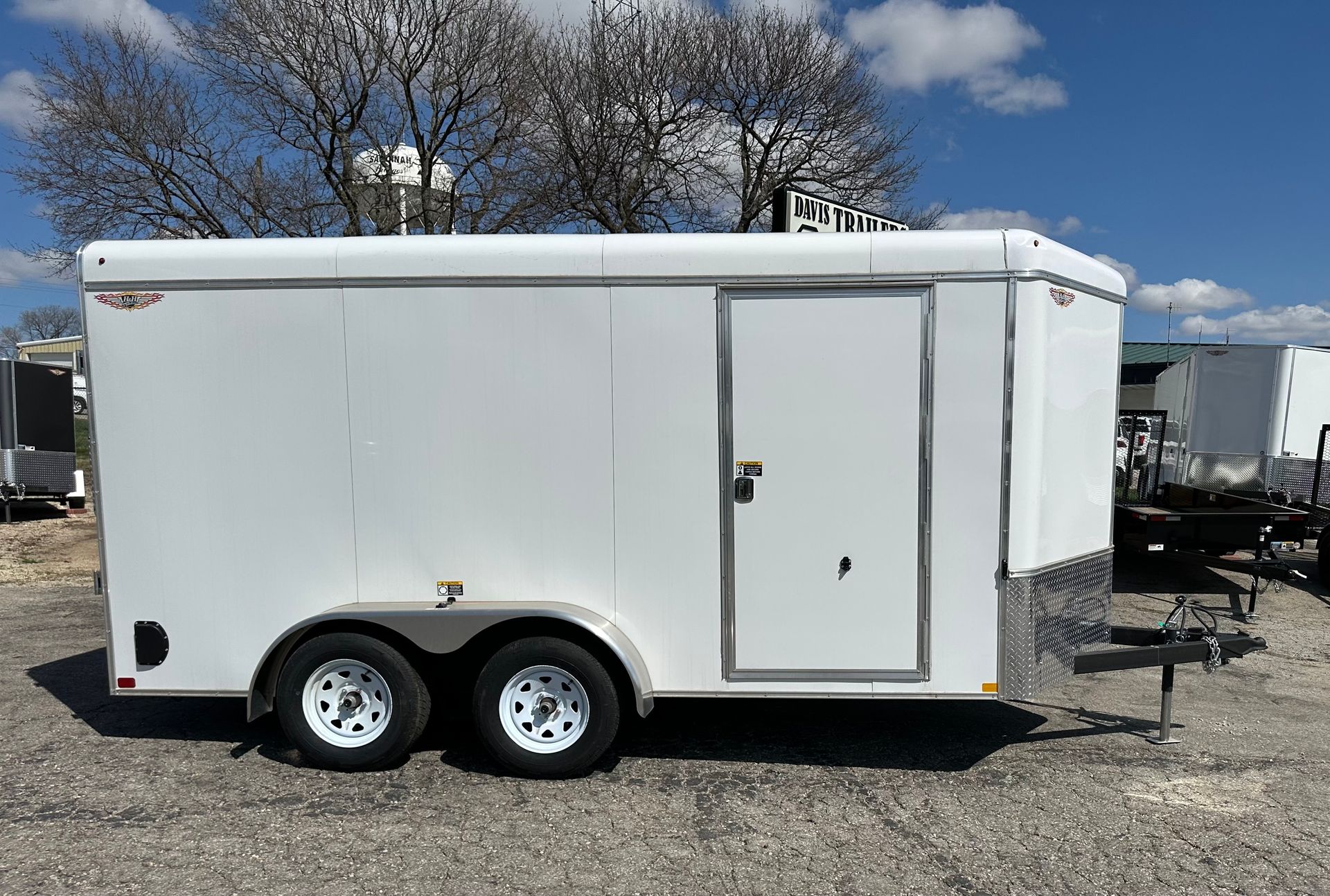 A trailer is parked in a gravel lot in front of a building.