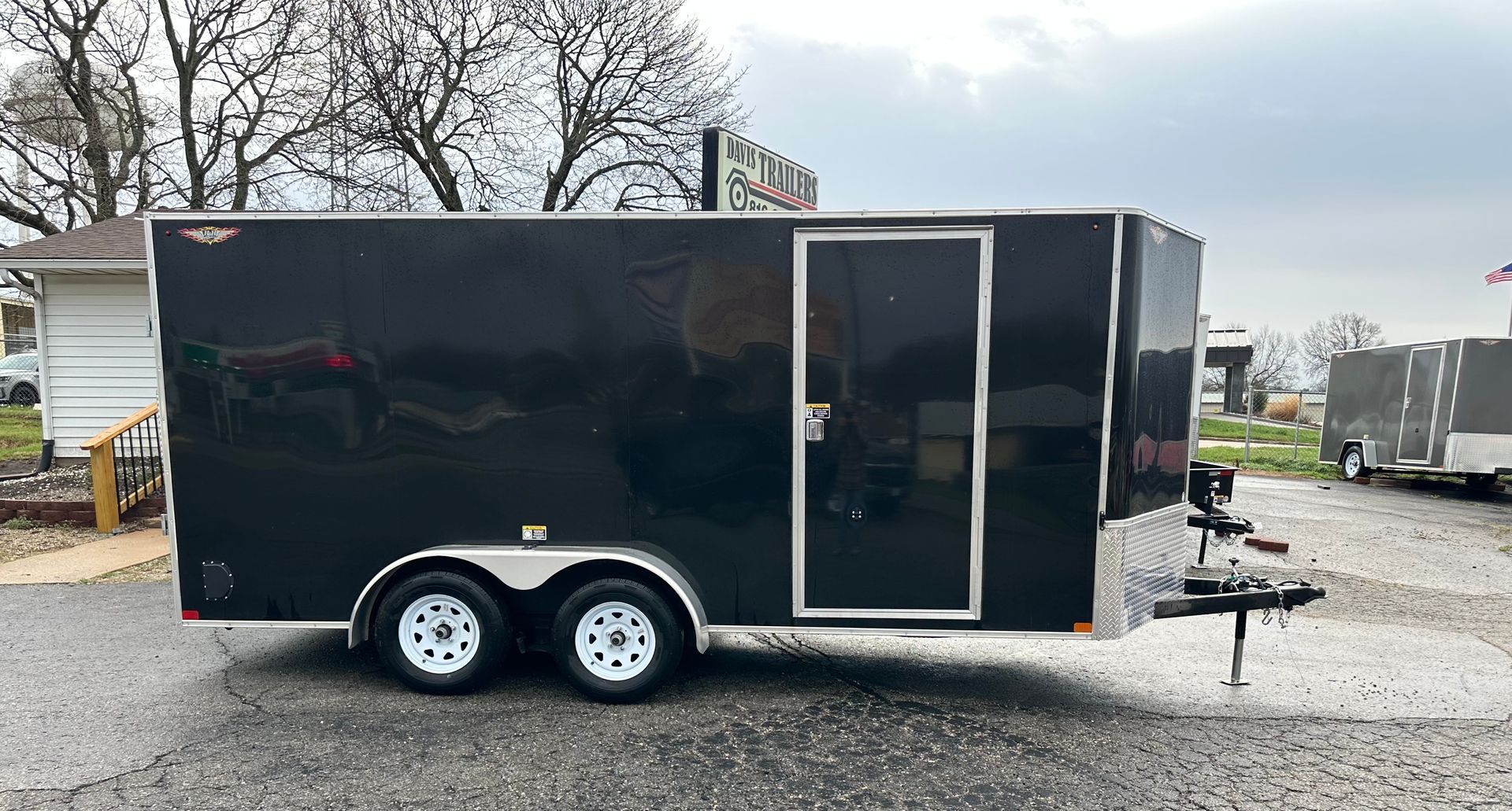 A white trailer is parked in a gravel lot next to a garage.