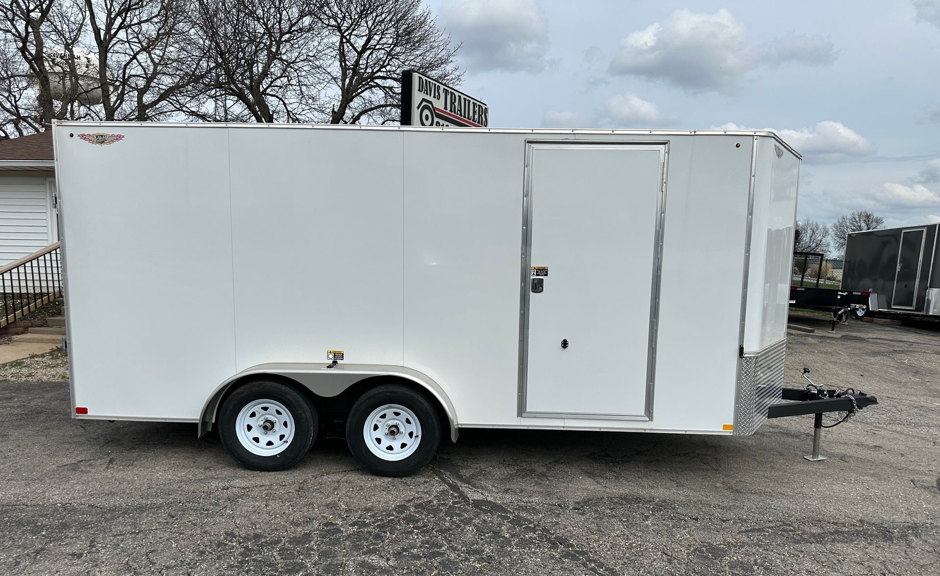 A gray trailer is parked in a gravel lot in front of a building.