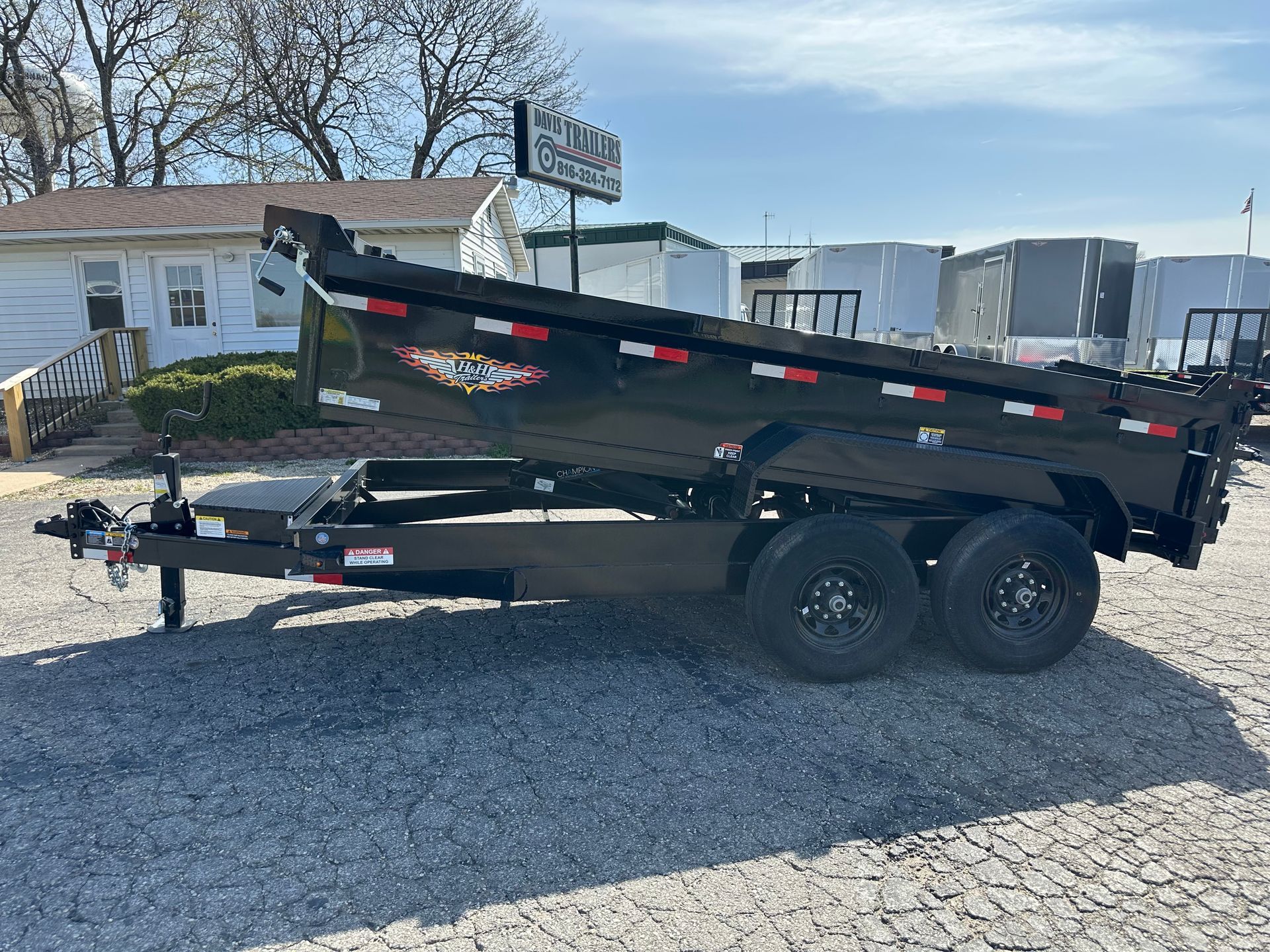 A black dump trailer is parked in a gravel lot.