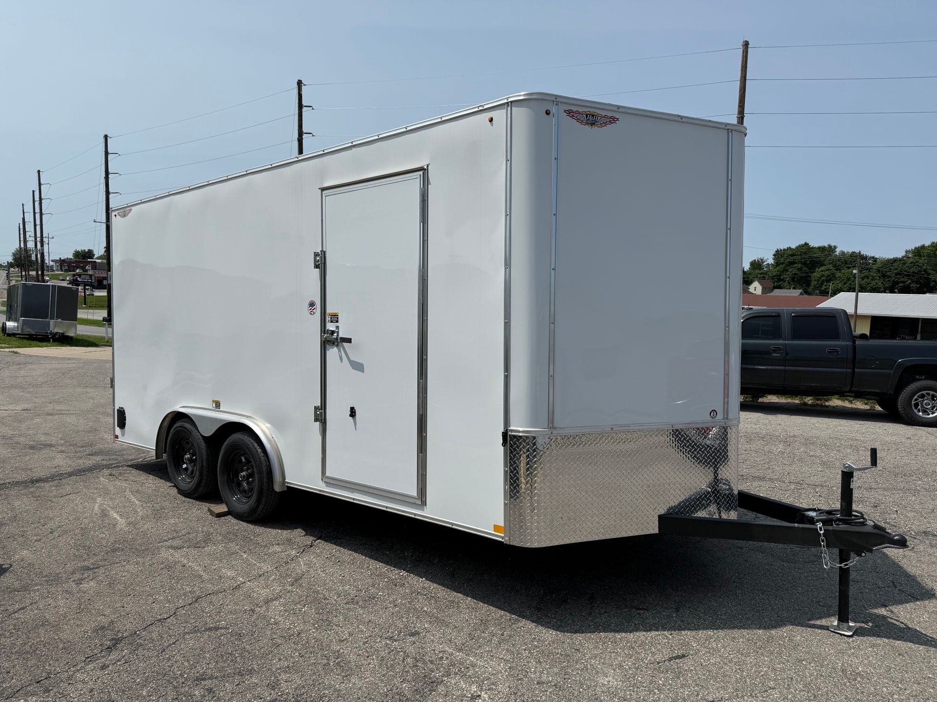 A white trailer is parked in a gravel lot next to a garage.