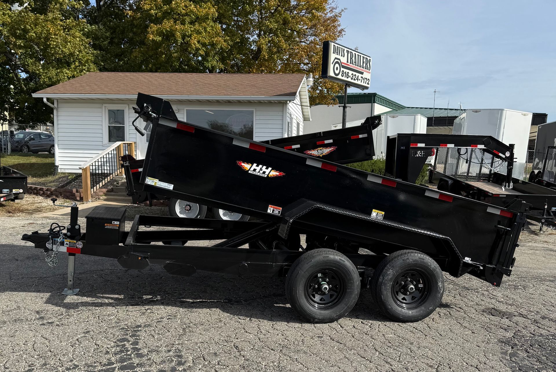 A black dump trailer is parked in a gravel lot.