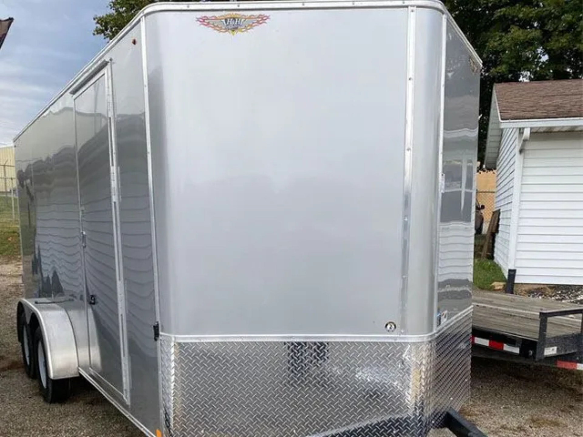 A white trailer is parked in a gravel lot next to a garage.