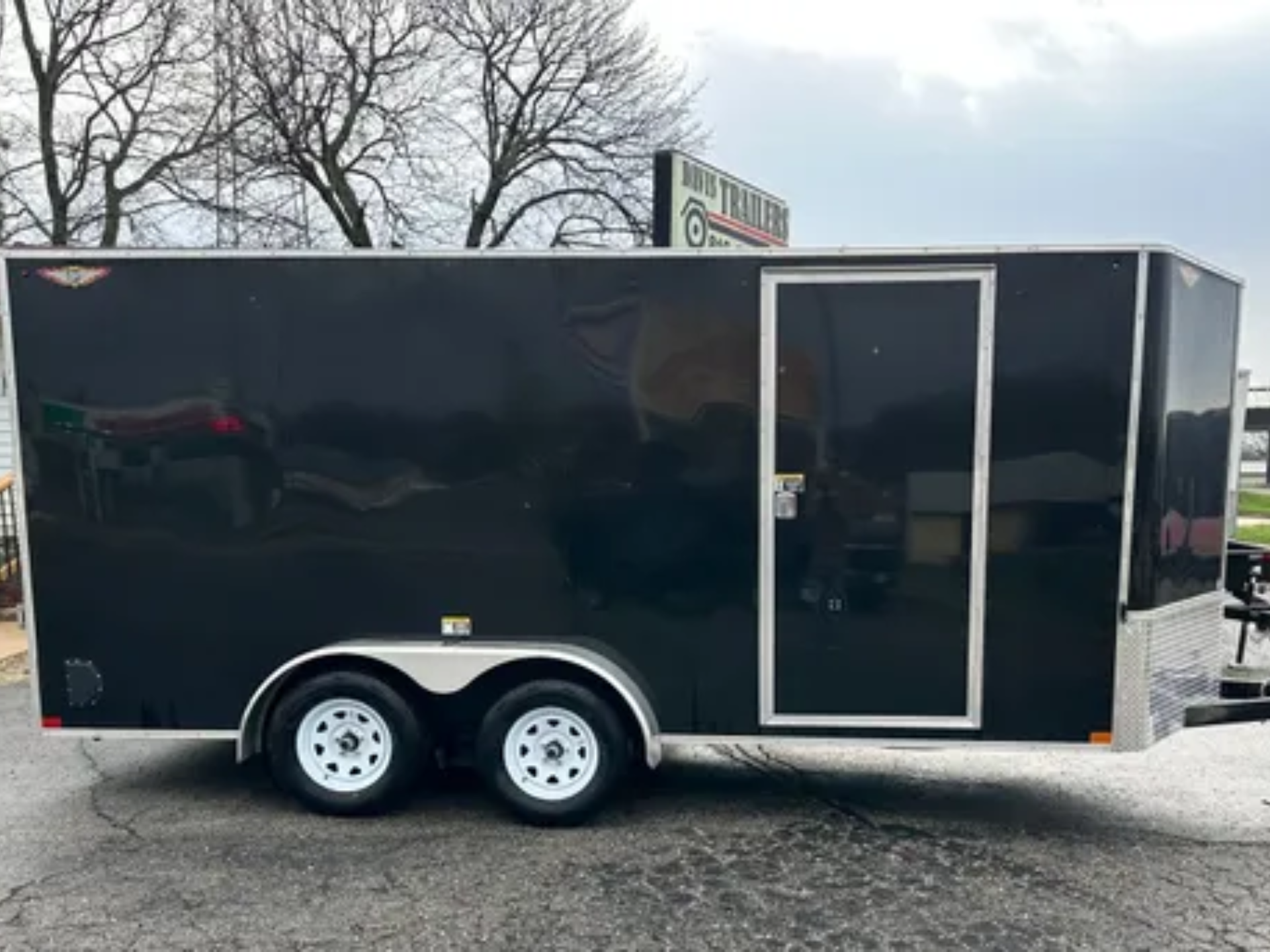 A trailer is parked in a gravel lot next to a garage.