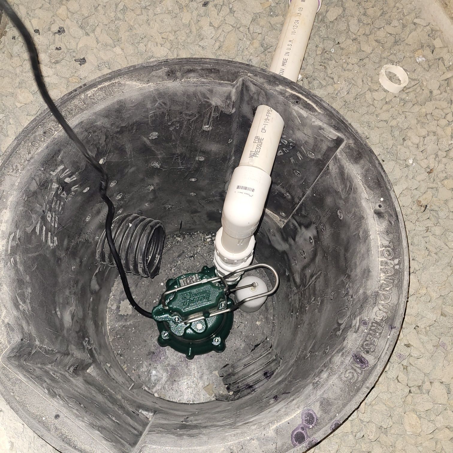 A green pump is sitting in the bottom of a basement drain.