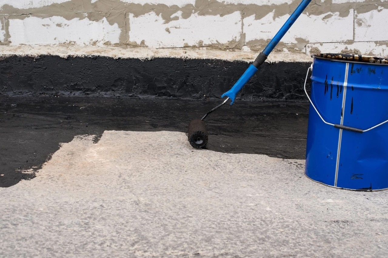 A roller is being used to paint a concrete surface next to a blue bucket.