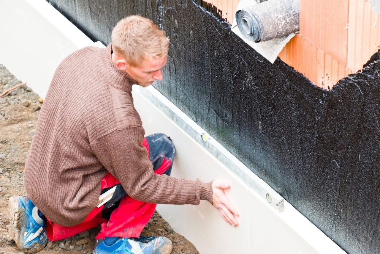 A man is kneeling down and painting a wall.