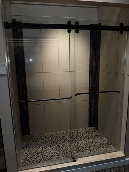 A shower stall with sliding glass doors and black handles