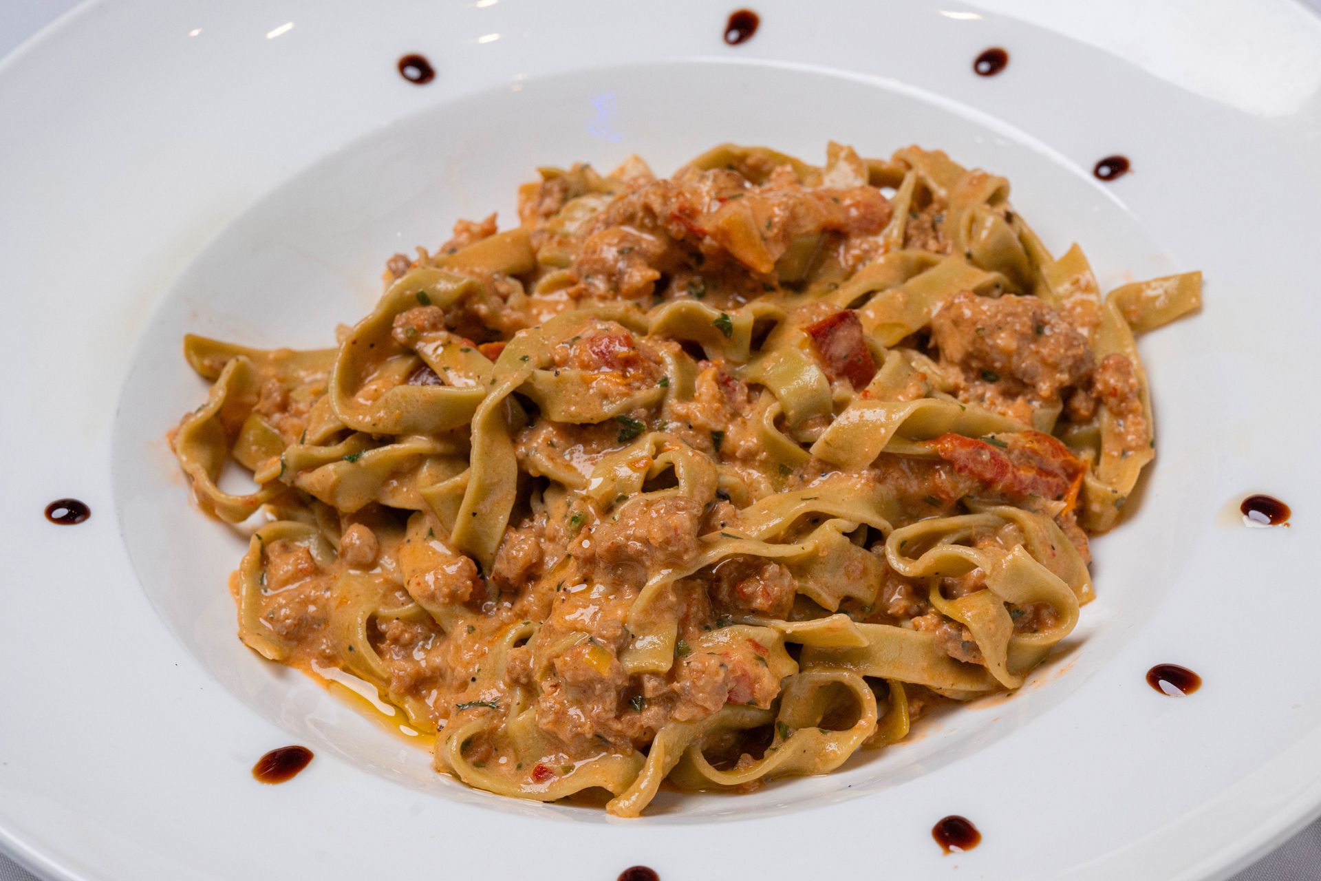Fettuccine pasta with rich, red meat sauce, garnished with fresh basil, served in a white bowl.