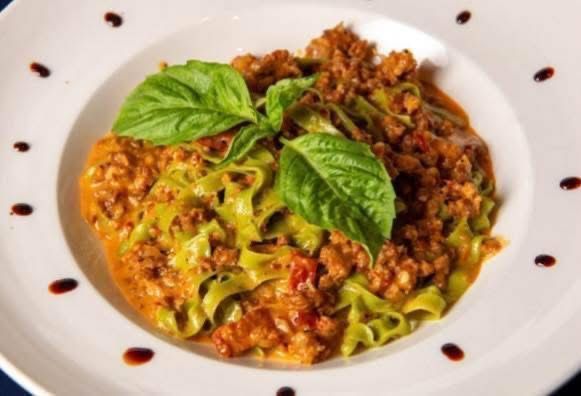 Pasta dish with green noodles, meat sauce, basil garnish, and decorative balsamic glaze.